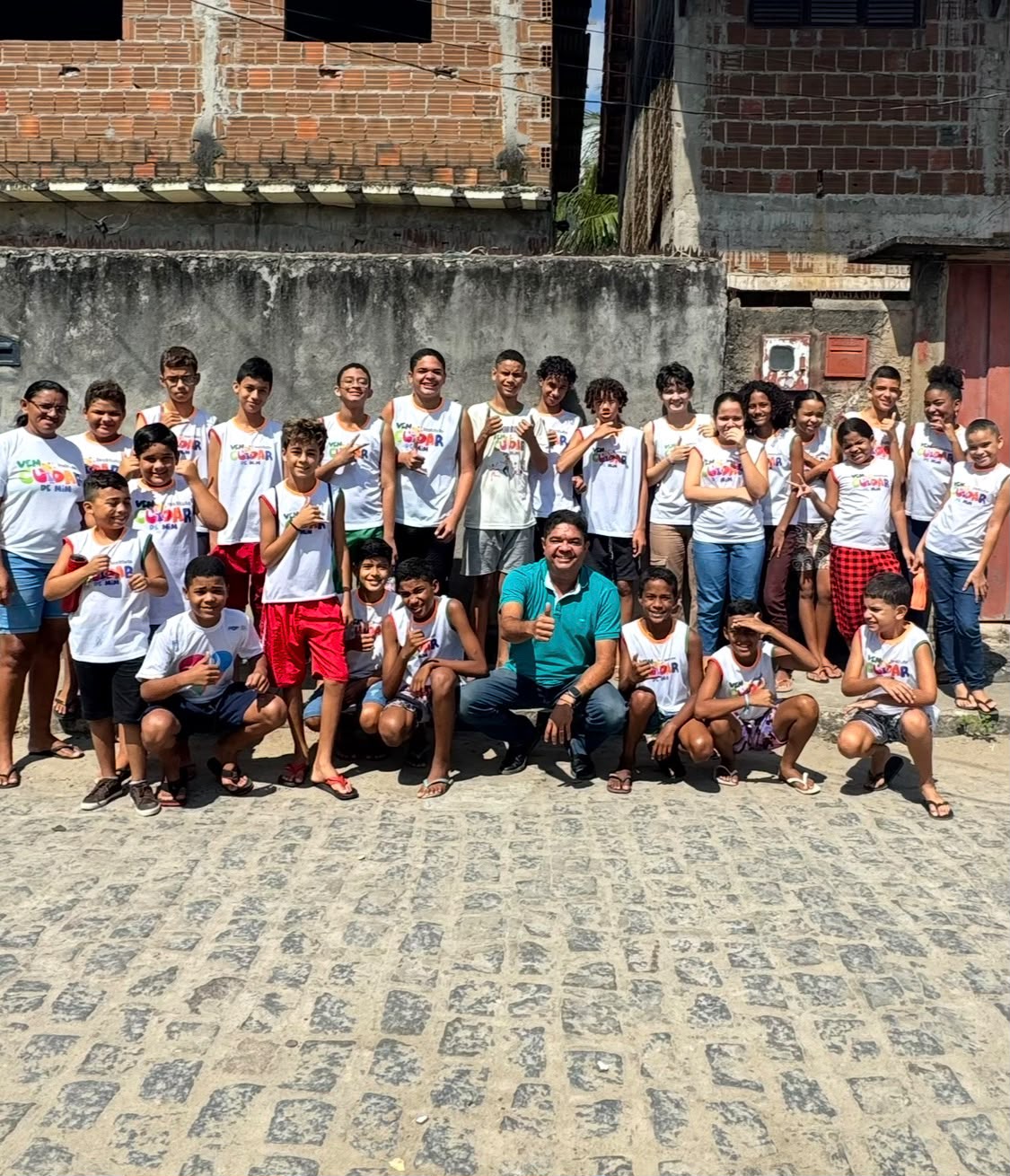 Cerca de trinta crianças e adolescentes do Instituto posando na rua de paralelepípedo da comunidade do Timbó, junto do fundador
